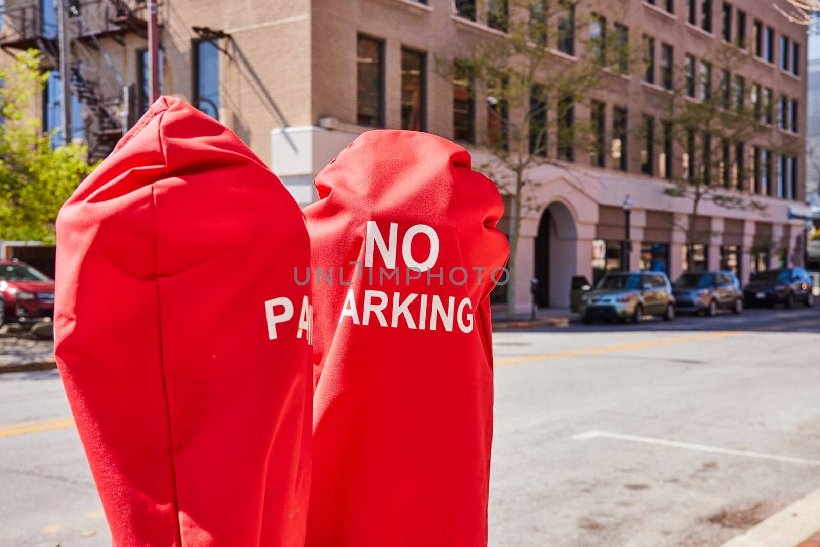Vibrant red NO PARKING meter covers on a sunny downtown Fort Wayne street, showcasing urban life and regulation.