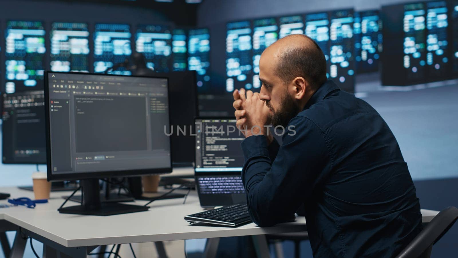 Man in server room typing code on laptop and PC by DCStudio