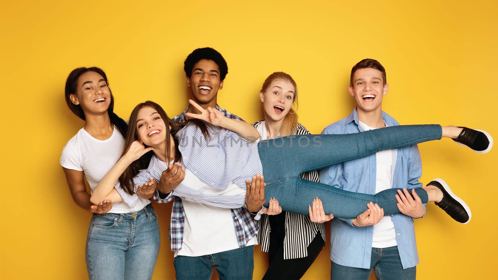 A diverse group of teenagers is seen gathering together and striking various poses in front of a camera, creating a lively and engaging atmosphere, holding their friend