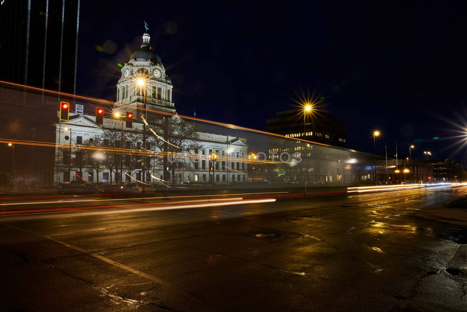 Fort Wayne's historic courthouse glows at night, contrasted by modern city lights and vibrant traffic streaks.