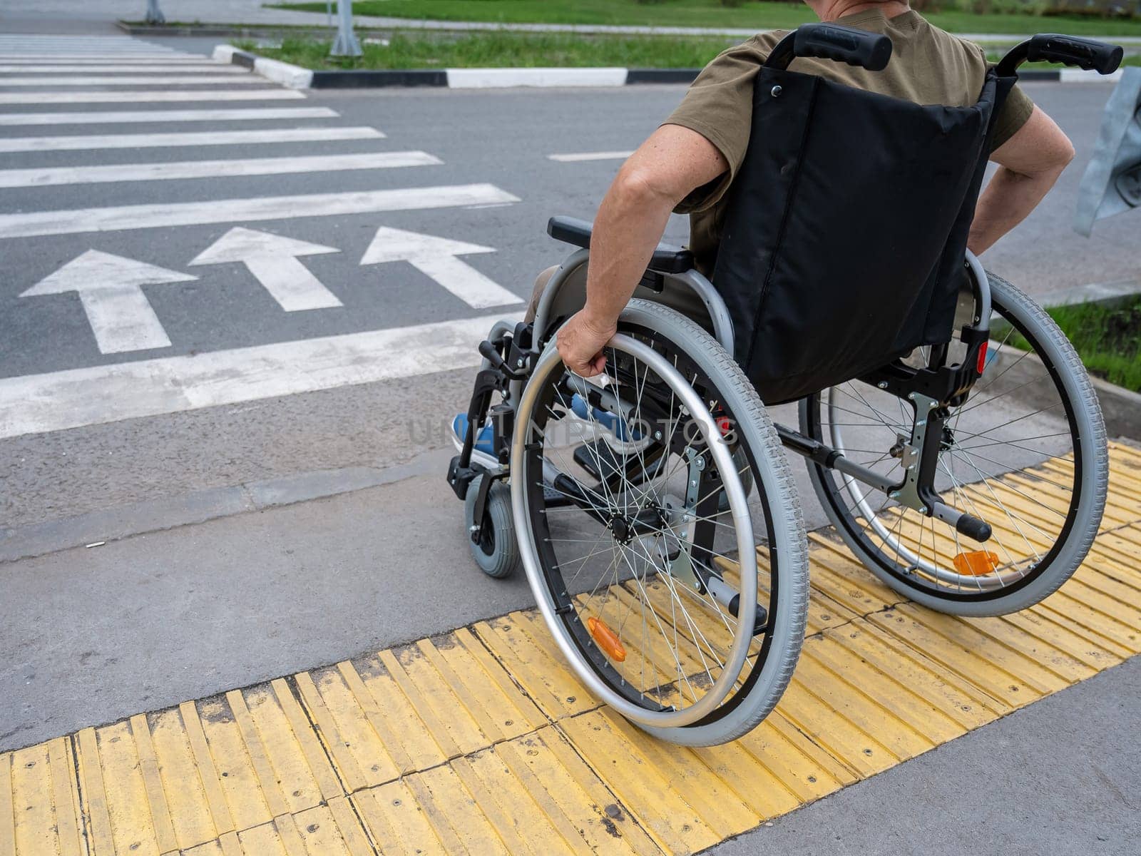 Rear view of an elderly woman in a wheelchair going to a pedestrian crossing. Close-up on wheels