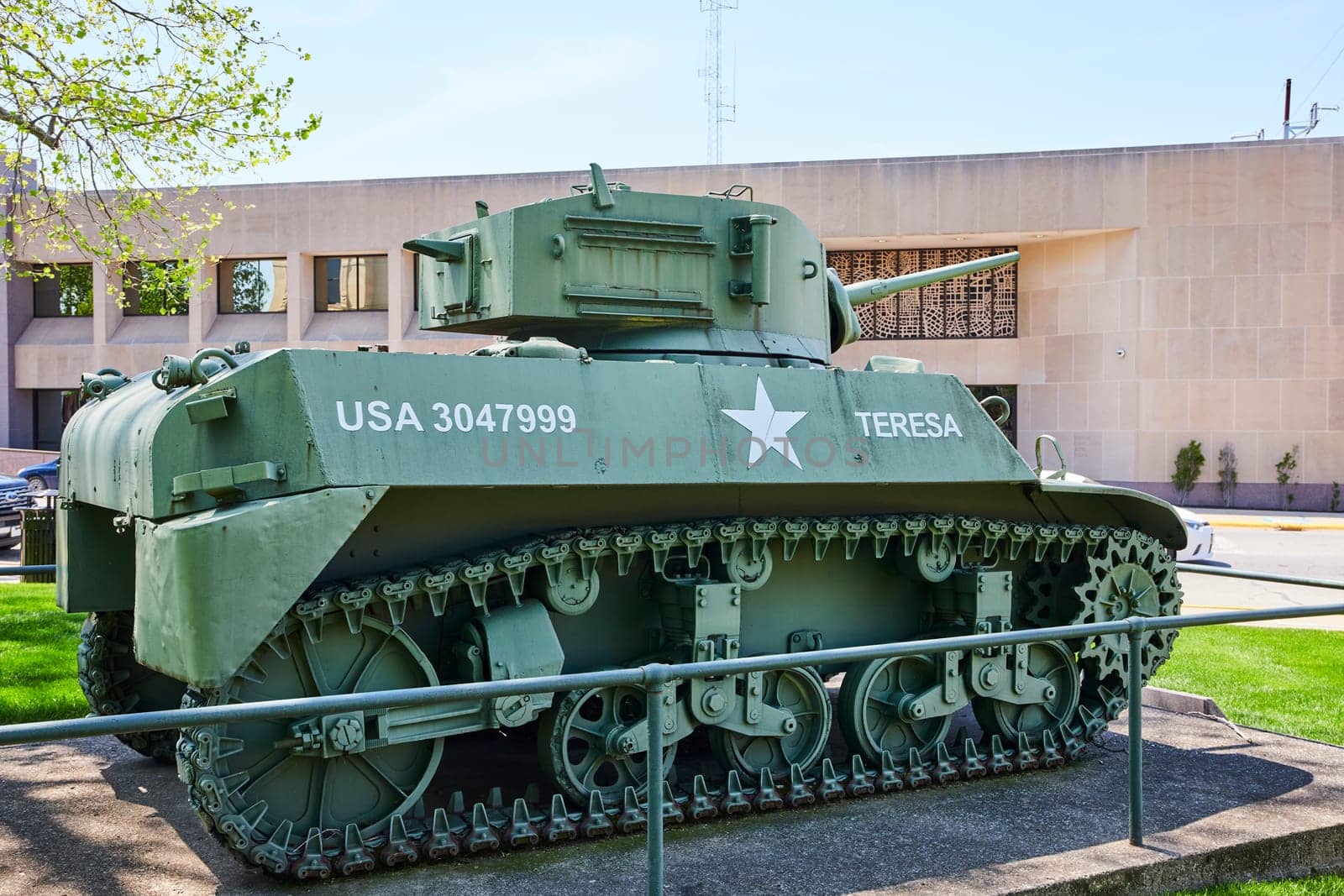 Vintage USA military tank 'TERESA' in contrast with modern office in Warsaw, Indiana, under clear skies.