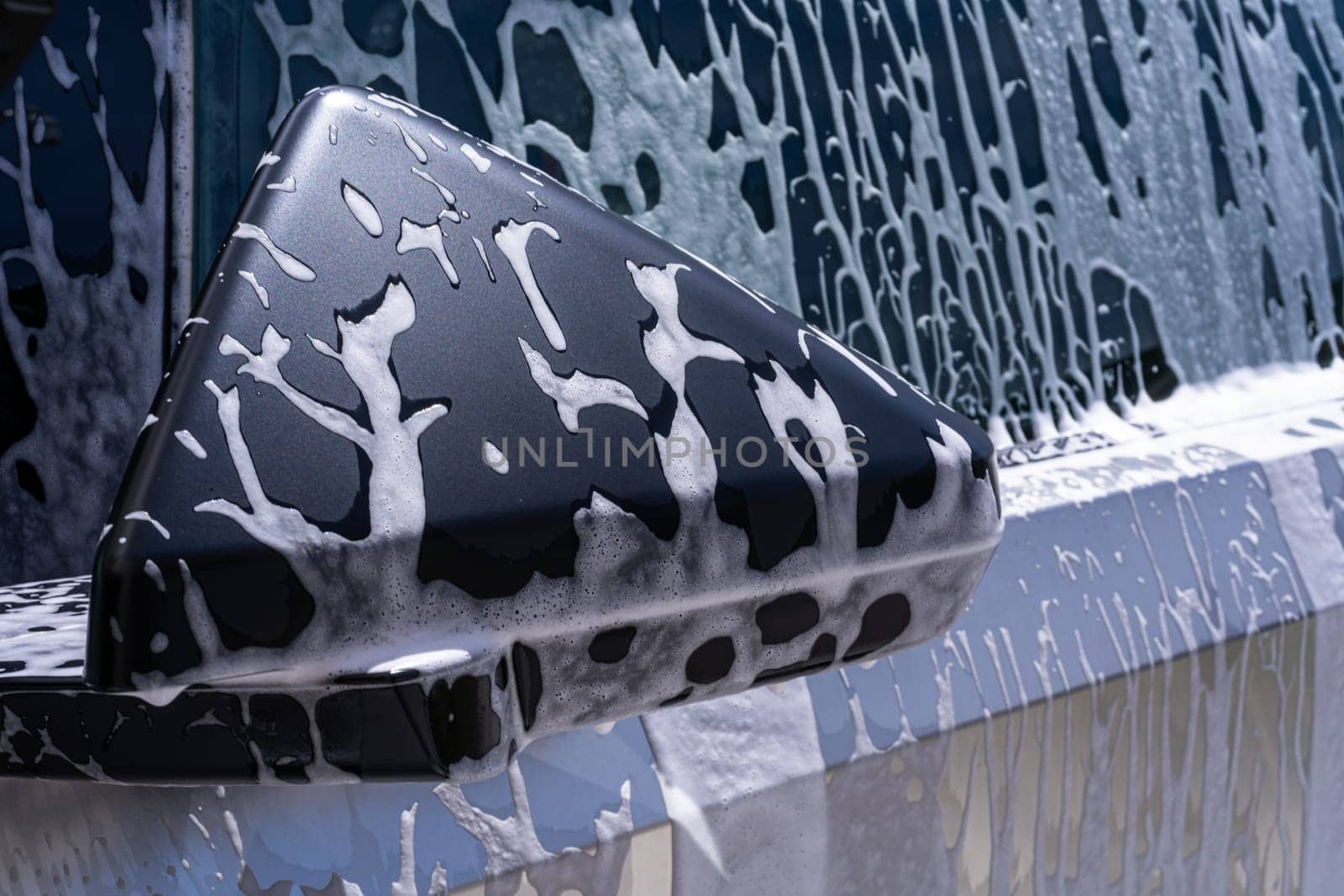 Denver, Colorado, USA-May 5, 2024-This image captures a close-up view of the Tesla Cybertruck side mirror covered in soap suds during a car wash, emphasizing the vehicle unique angular design and rugged exterior.