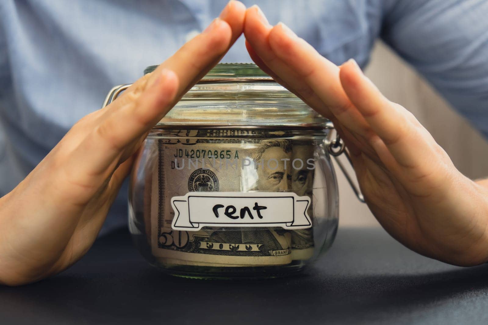 Unrecognizable woman holding Saving Money In Glass Jar filled with Dollars banknotes. RENT transcription in front of jar. Managing personal finances extra income for future insecurity background