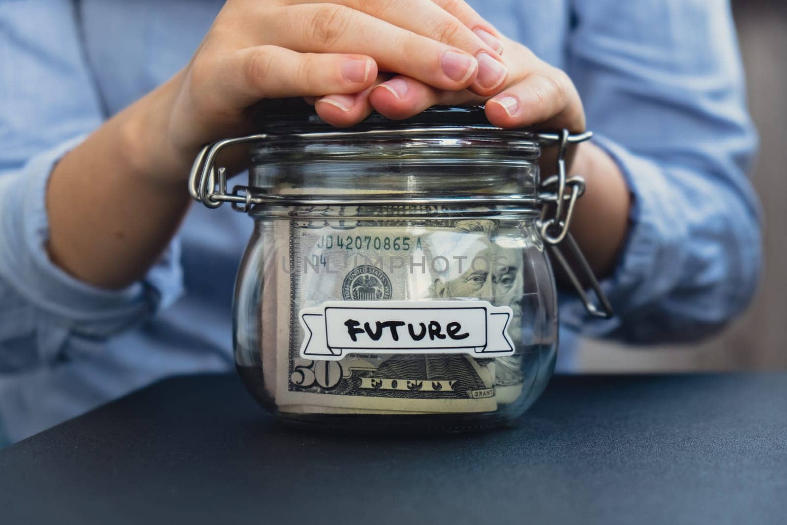 Female hands Saving Money In Glass Jar filled with Dollars banknotes. FUTURE transcription in front of jar. Managing personal finances extra income for future insecurity by anna_stasiia