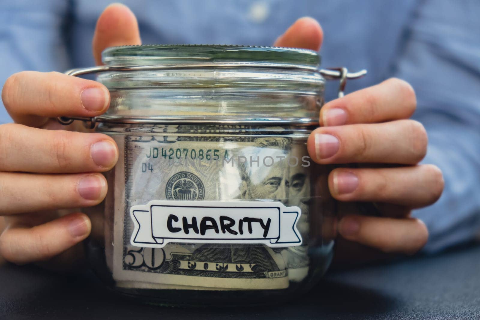 Unrecognizable woman holding Glass jar full of American currency dollars cash banknote with text CHARITY. Preparation saving money. Moderate consumption and economy. Collecting money