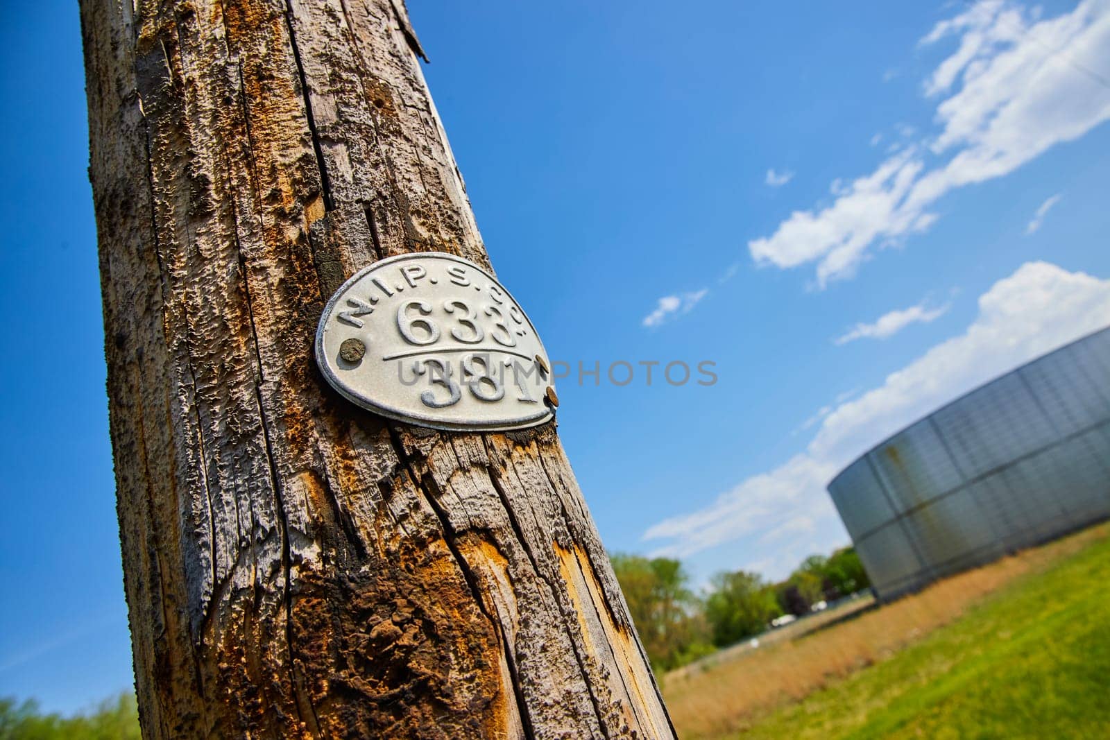 Rustic NIPSCO utility pole, tagged '633 381', stands against a clear sky near industrial Warsaw, Indiana.