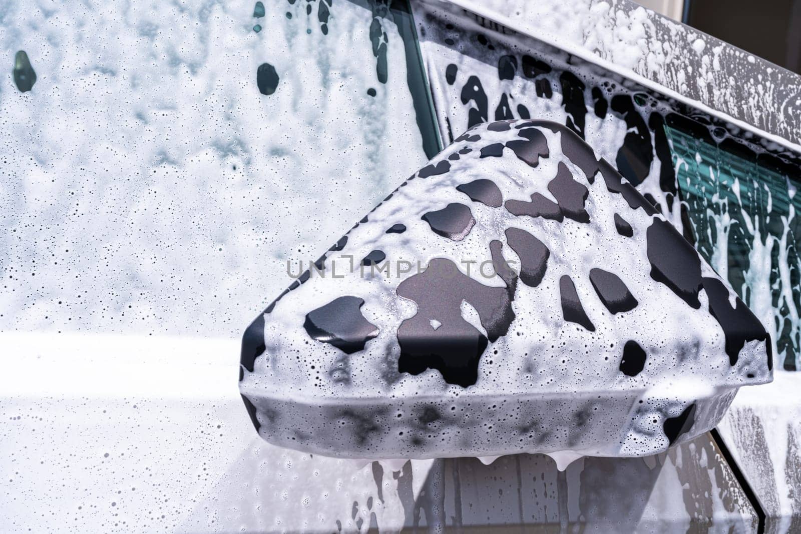 Denver, Colorado, USA-May 5, 2024-This image captures a close-up view of the Tesla Cybertruck side mirror covered in soap suds during a car wash, emphasizing the vehicle unique angular design and rugged exterior.