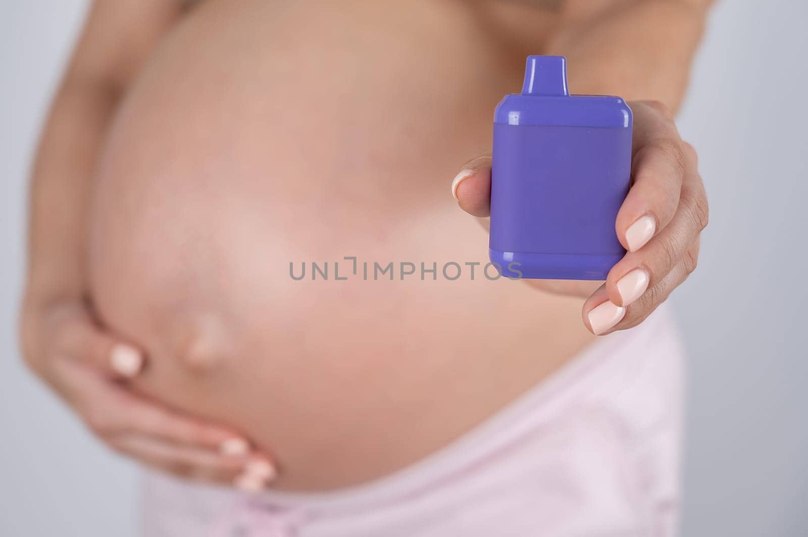 A pregnant woman smokes a vape. A girl holds an electronic cigarette against the background of her bare tummy. by mrwed54