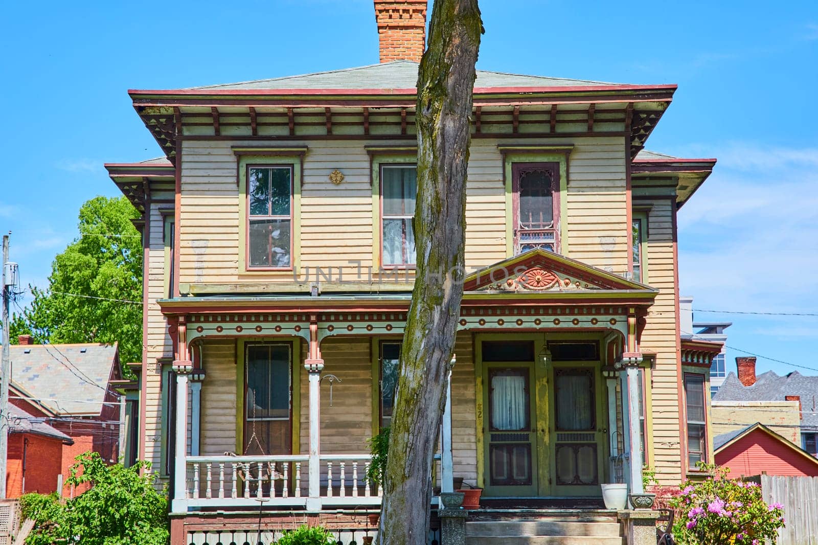 Victorian charm in Fort Wayne: A historic home with ornate trimmings and a weathered tree, set against a clear blue sky.