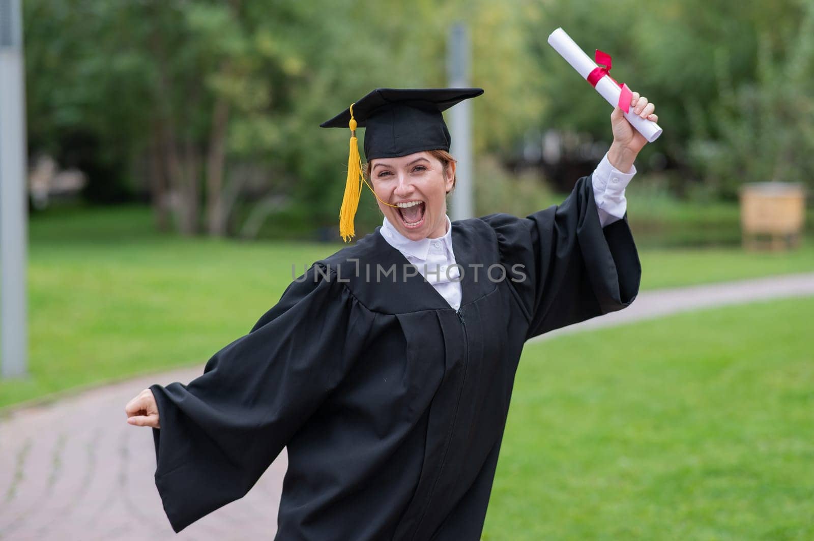 Caucasian woman in graduate gown dancing for joy outdoors. by mrwed54
