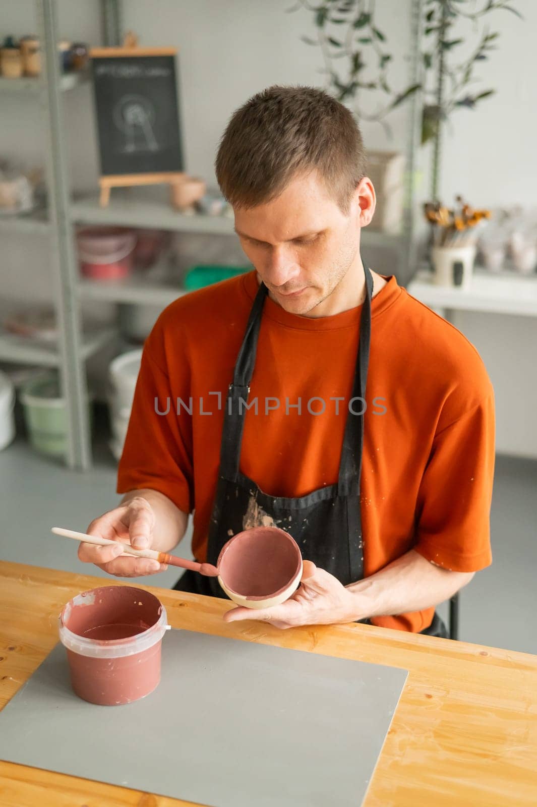 Potter paints ceramic dishes with a brush. Vertical photo