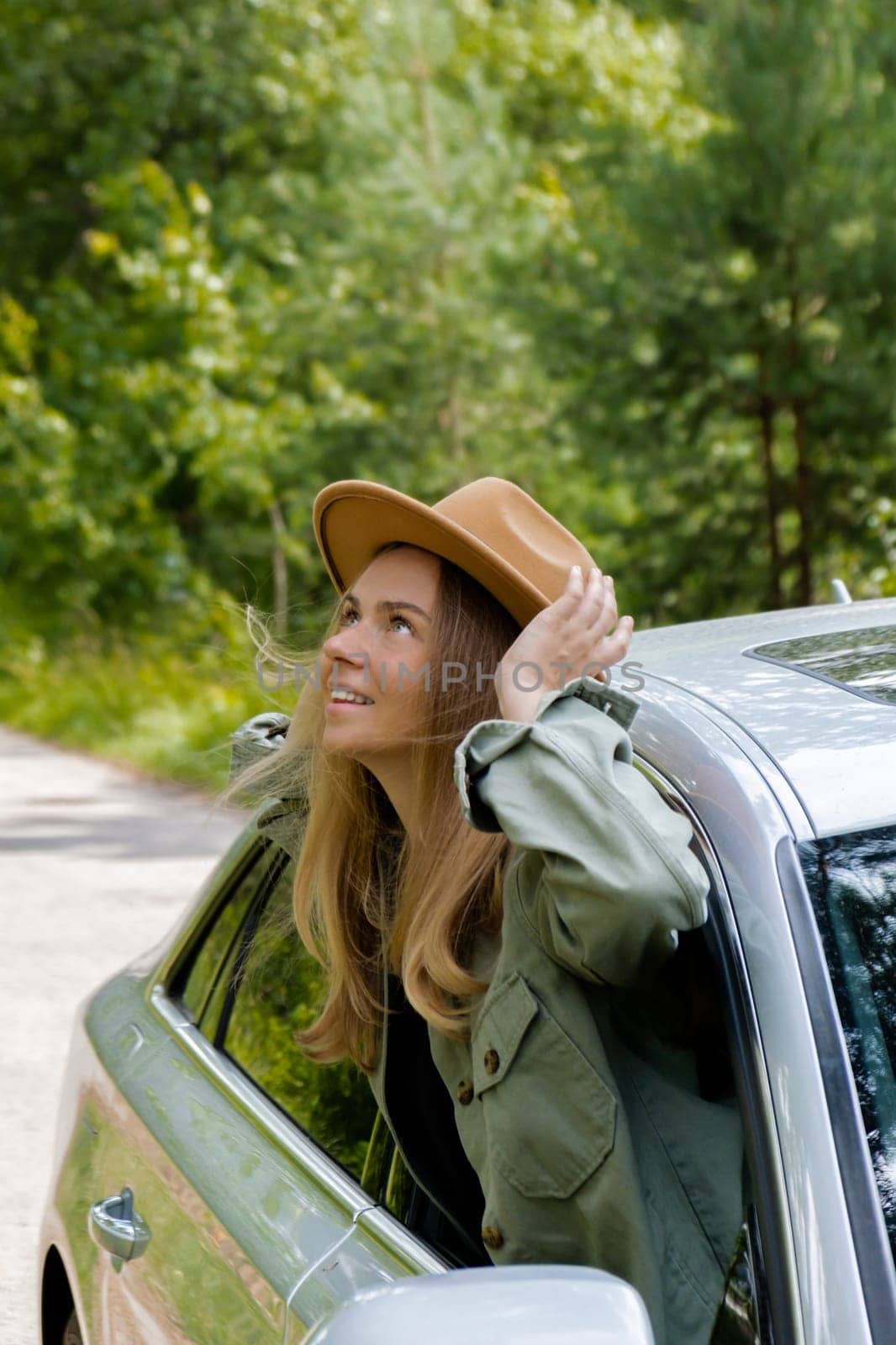 Blonde woman in hat sticking head out of windshield car. Young tourist explore local travel making candid real moments. True emotions expressions of getting away and refresh relax on open clean air