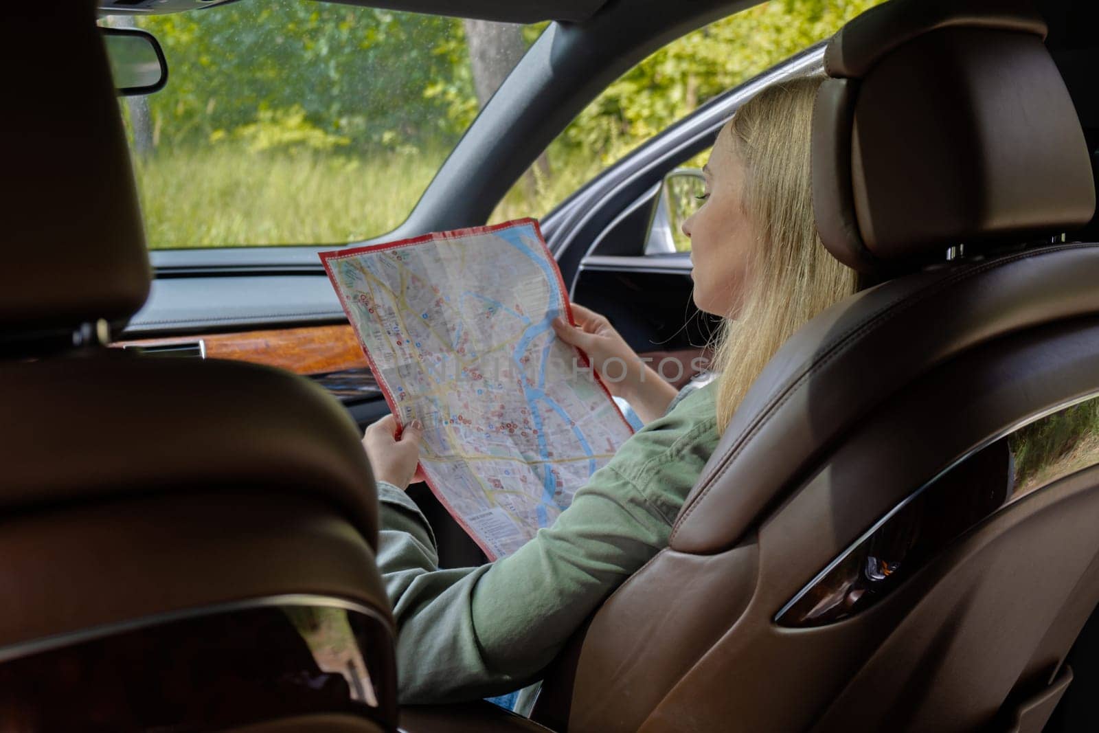 Smiling young woman sitting in car on road check the route on travel map. Local solo travel on weekends concept. Exited woman explore freedom outdoors in forest. Unity with nature lifestyle, rest recharge relaxation