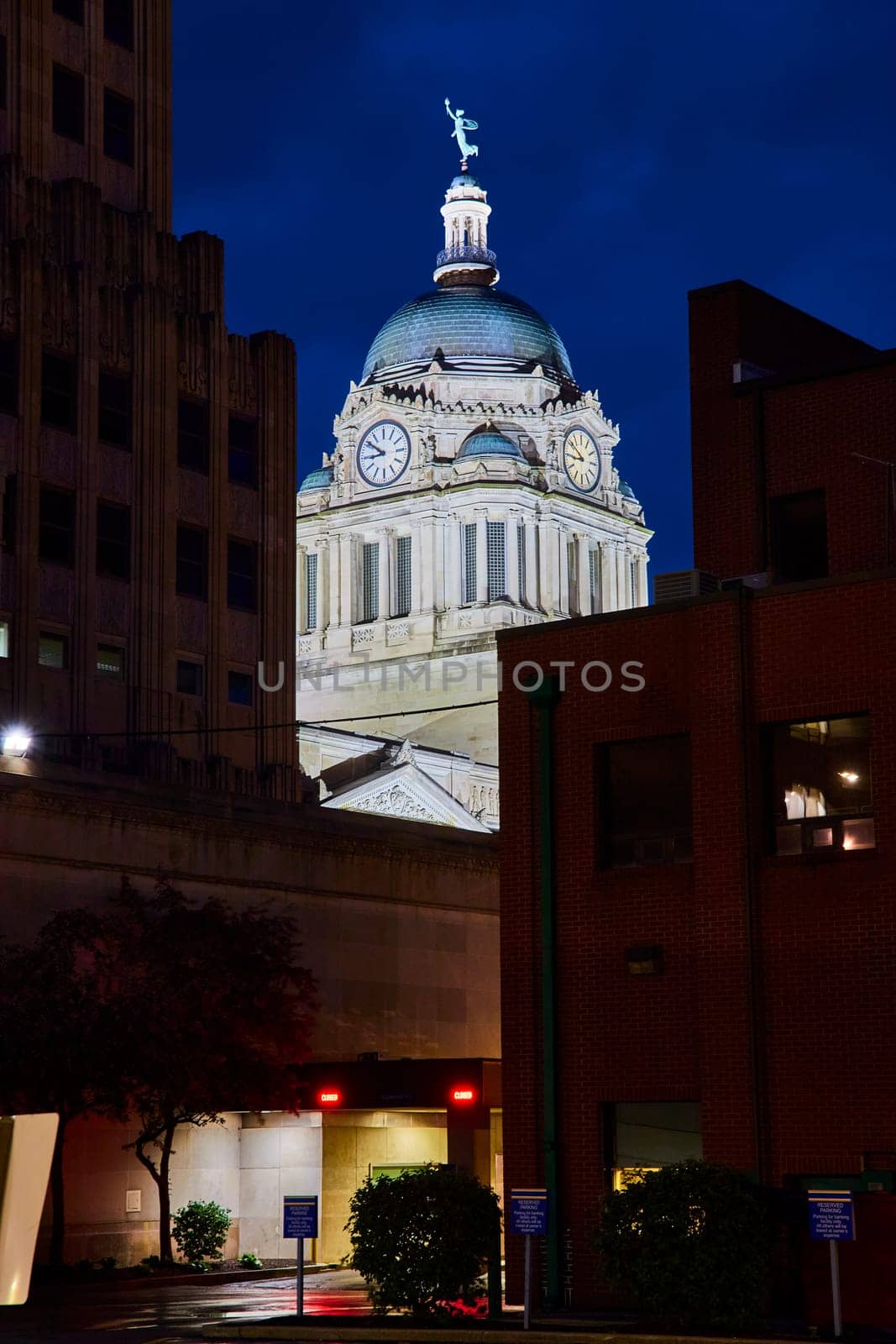 Illuminated Allen County Courthouse dome at night, flanked by modern buildings in downtown Fort Wayne.