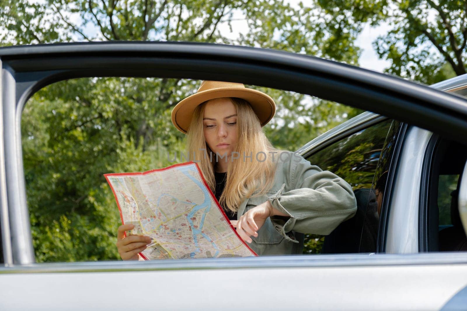 Smiling young woman in hat stoped on road to check the route on travel map. Local solo travel on weekends concept. Exited woman explore freedom outdoors in forest. Unity with nature lifestyle, rest recharge by anna_stasiia