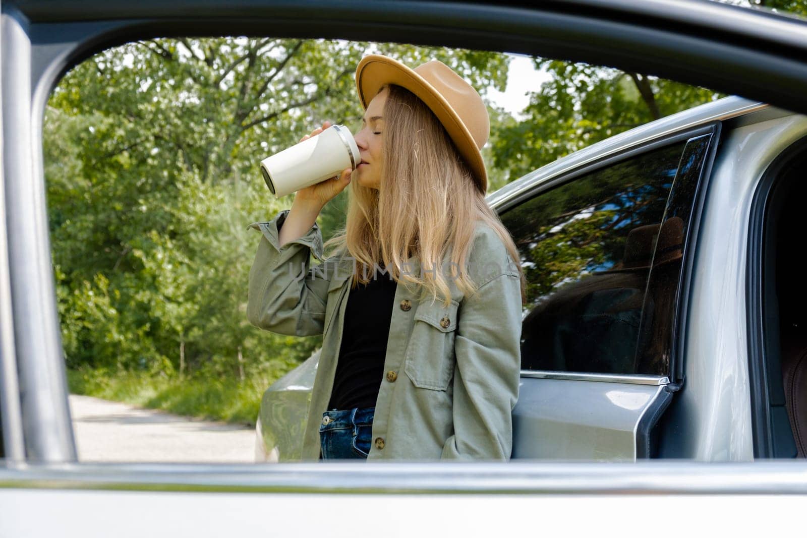 Smiling young woman drinking coffee or tea from reusable thermos cup. Traveler making a coffee break in Local solo travel on weekends concept. Exited woman explore freedom outdoors in forest. Unity with nature lifestyle, rest recharge relaxation