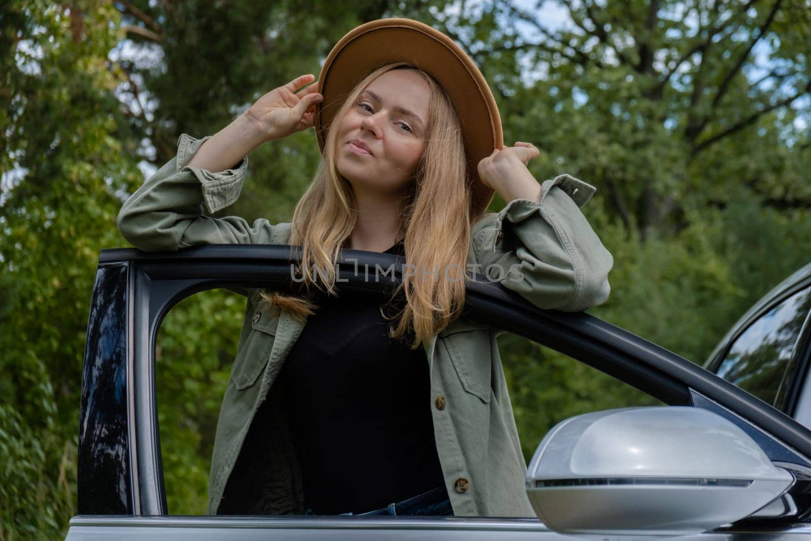 Blonde woman in hat staying next to car door. Young tourist explore local travel making candid real moments. True emotions expressions of getting away and refresh relax by anna_stasiia