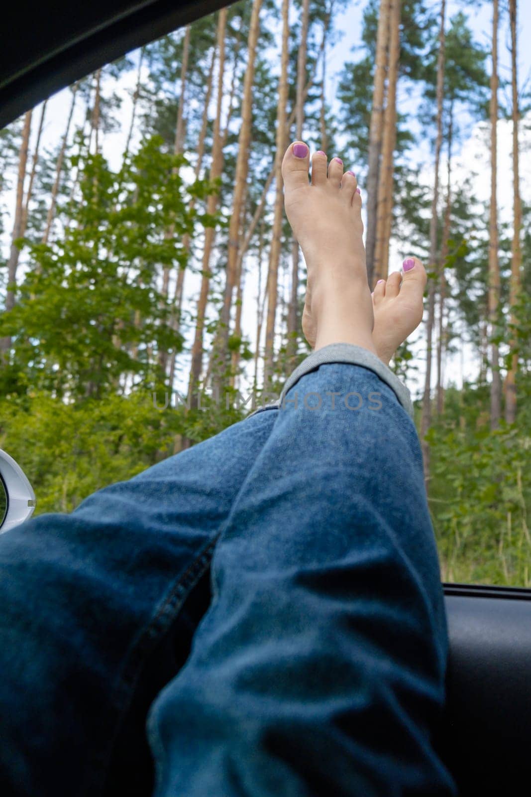 Female feet in blue jeans out of car window. Concept of comfortable travel vacation holiday. Getting away to make real candid moments. Reduce carbon footprint. Woman resting in road trip refresh and recharge