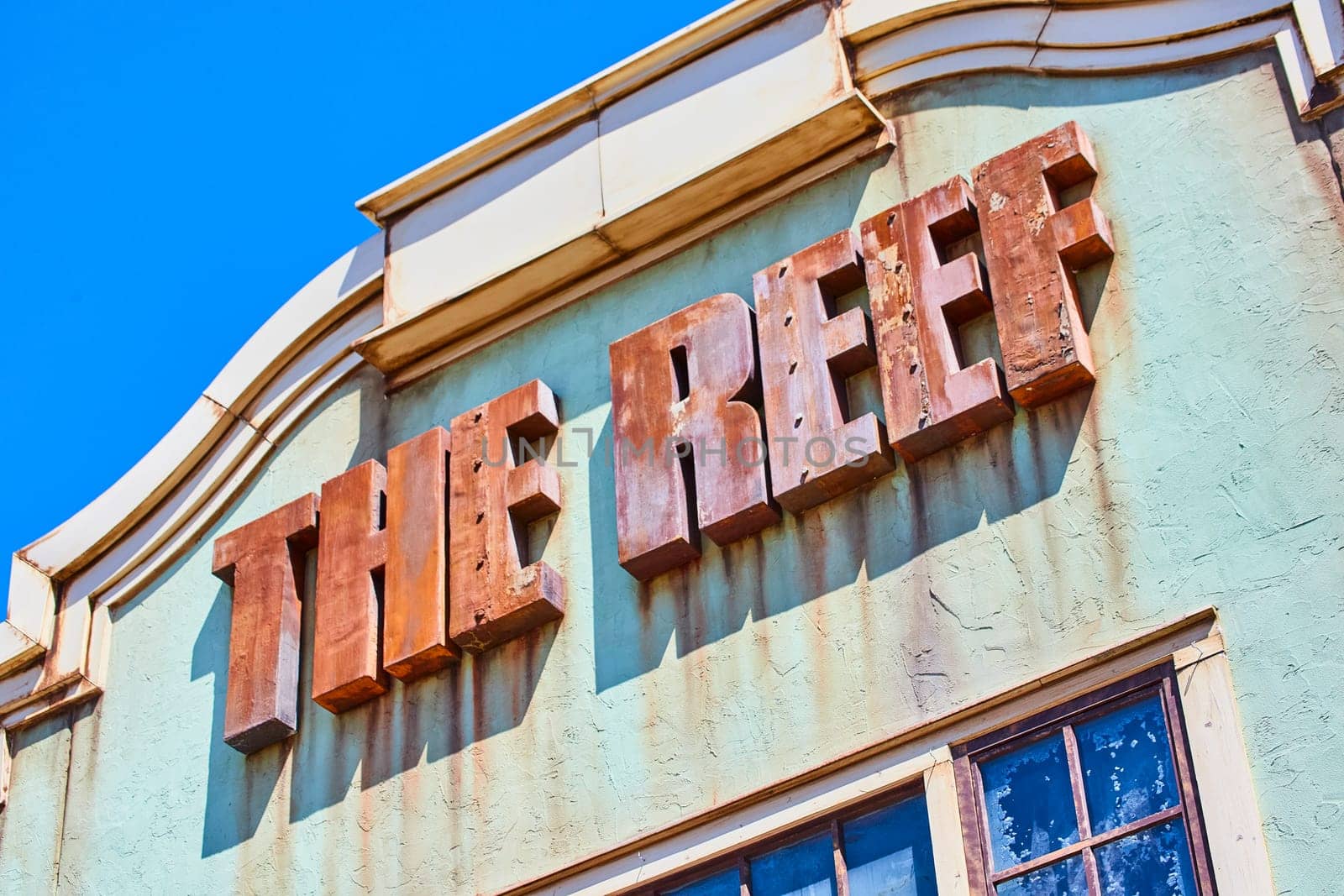Vintage 'THE REEF' sign on a rustic sea green wall, showcasing historical decay under bright daylight.