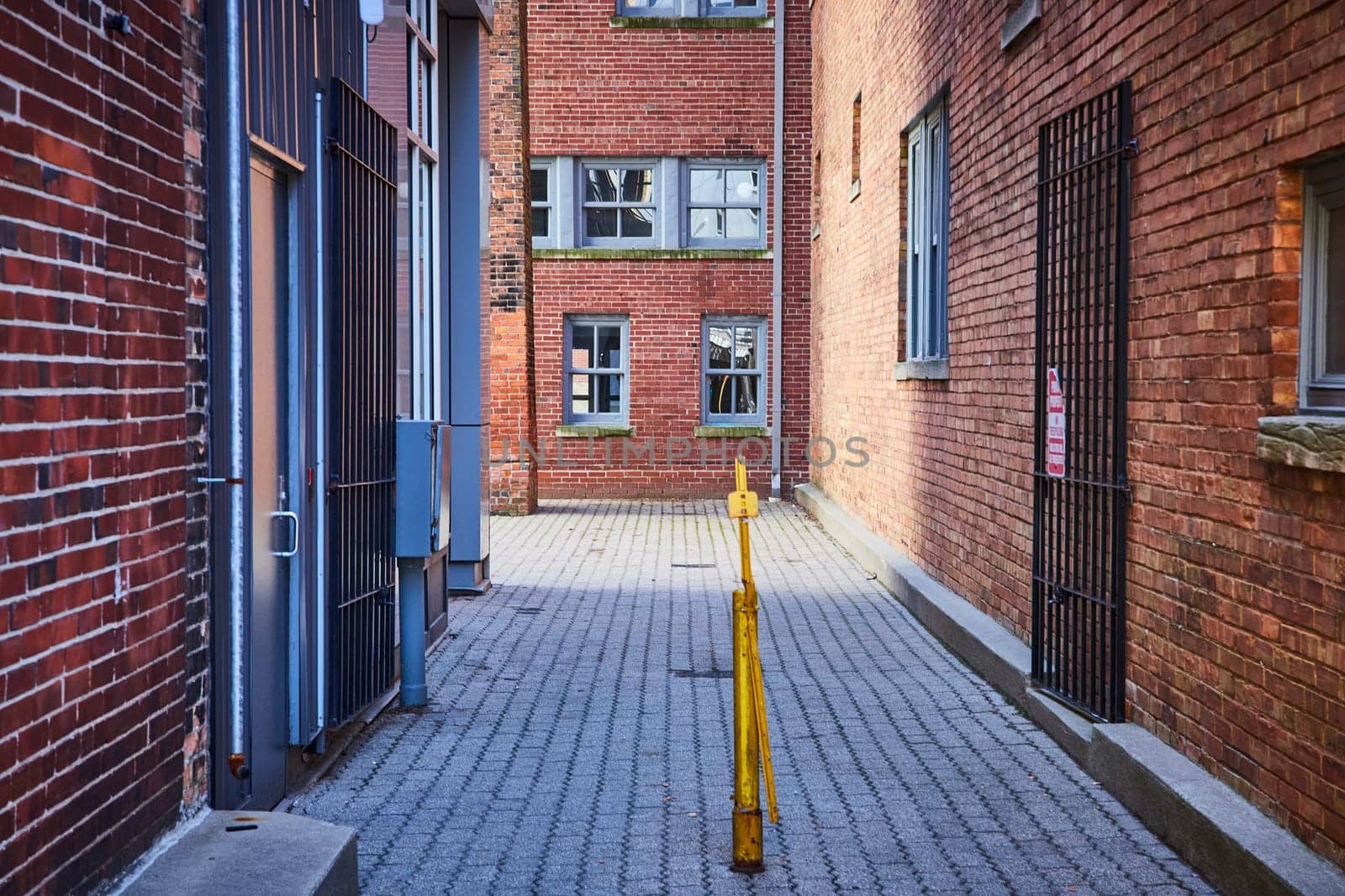 Historic alley in downtown Fort Wayne with rustic brick walls, large windows, and a striking yellow bollard.