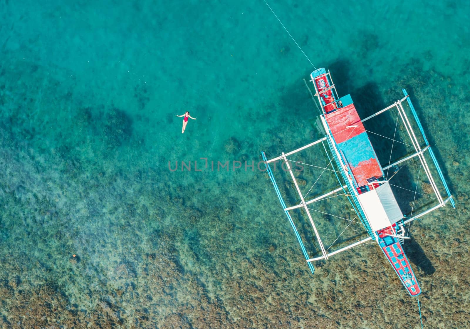 Aerial View of a Woman in Red Swimsuit Floating Serenely on the Crystal Clear Ocean Waters During Midday by Busker