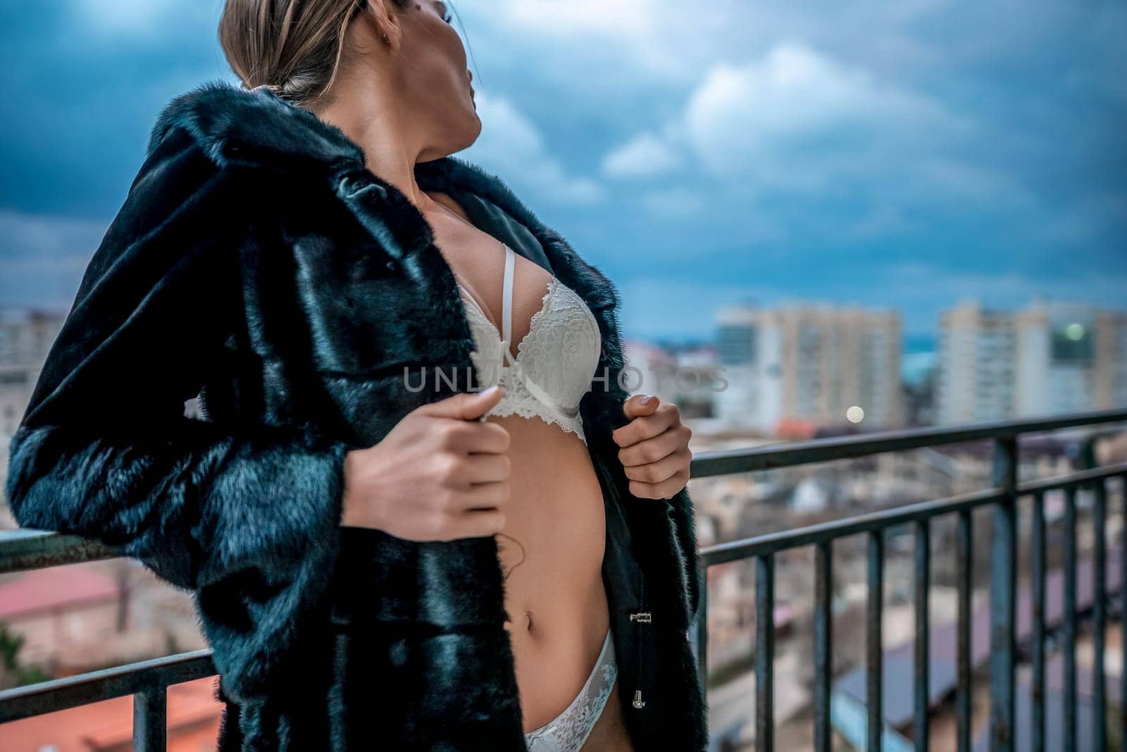 Unrecognizable Young sexy brunette woman in lingerie and fur coat staying on balcony and posing. Close-up of a woman's bust, frozen with goosebumps. Flirting of lovely female in hotel room. by panophotograph