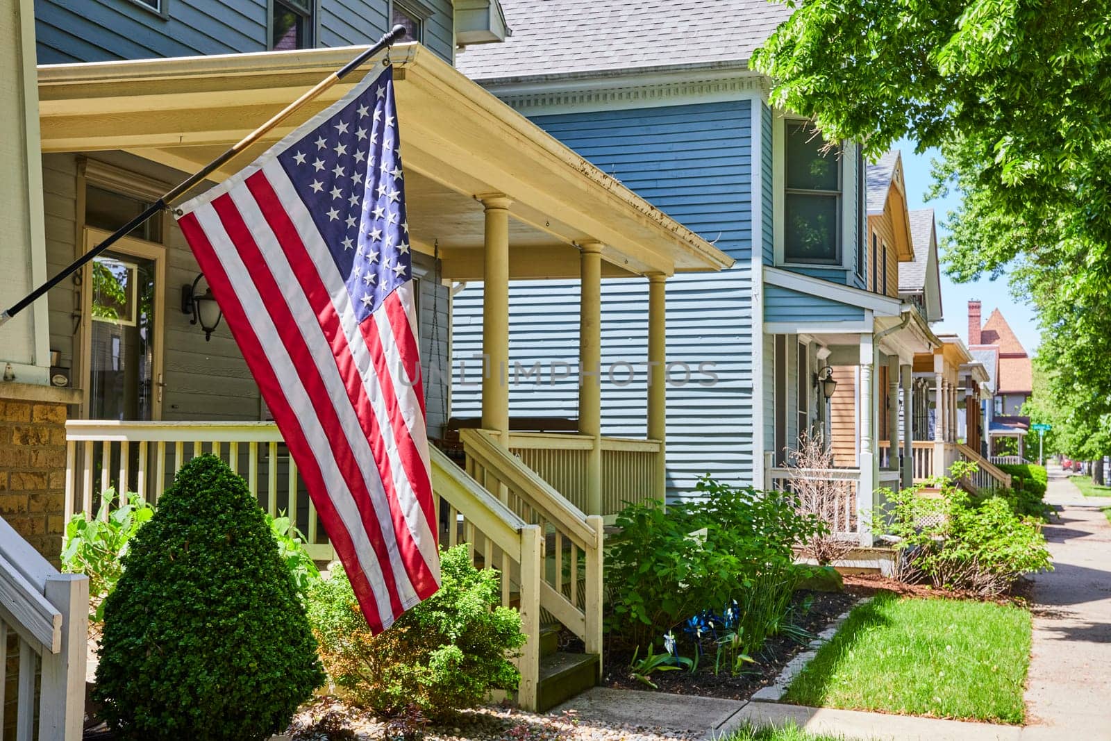 Sunny suburban street in Fort Wayne, USA, with homes displaying American flags, embodying community and patriotism.