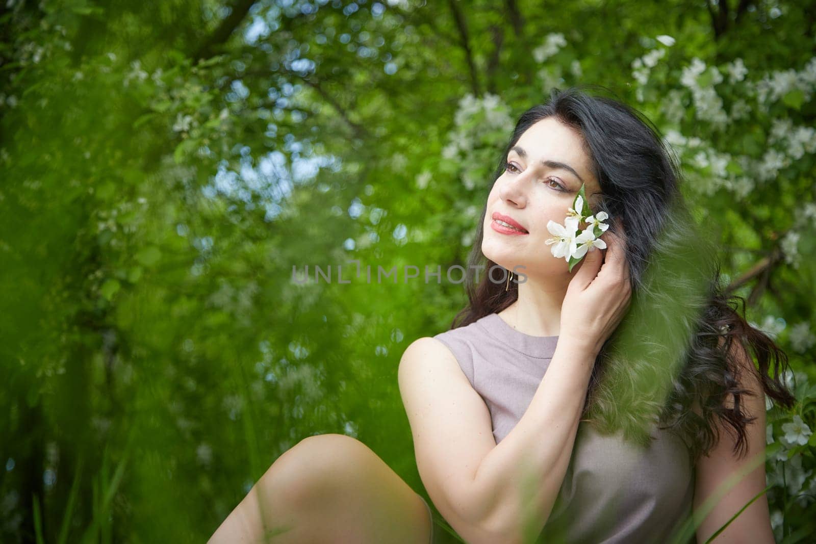 Joyous brunette woman near Blossoms of apple tree in a Spring Garden outdoors. Concept of face and body care. The scent of perfume and tenderness by keleny