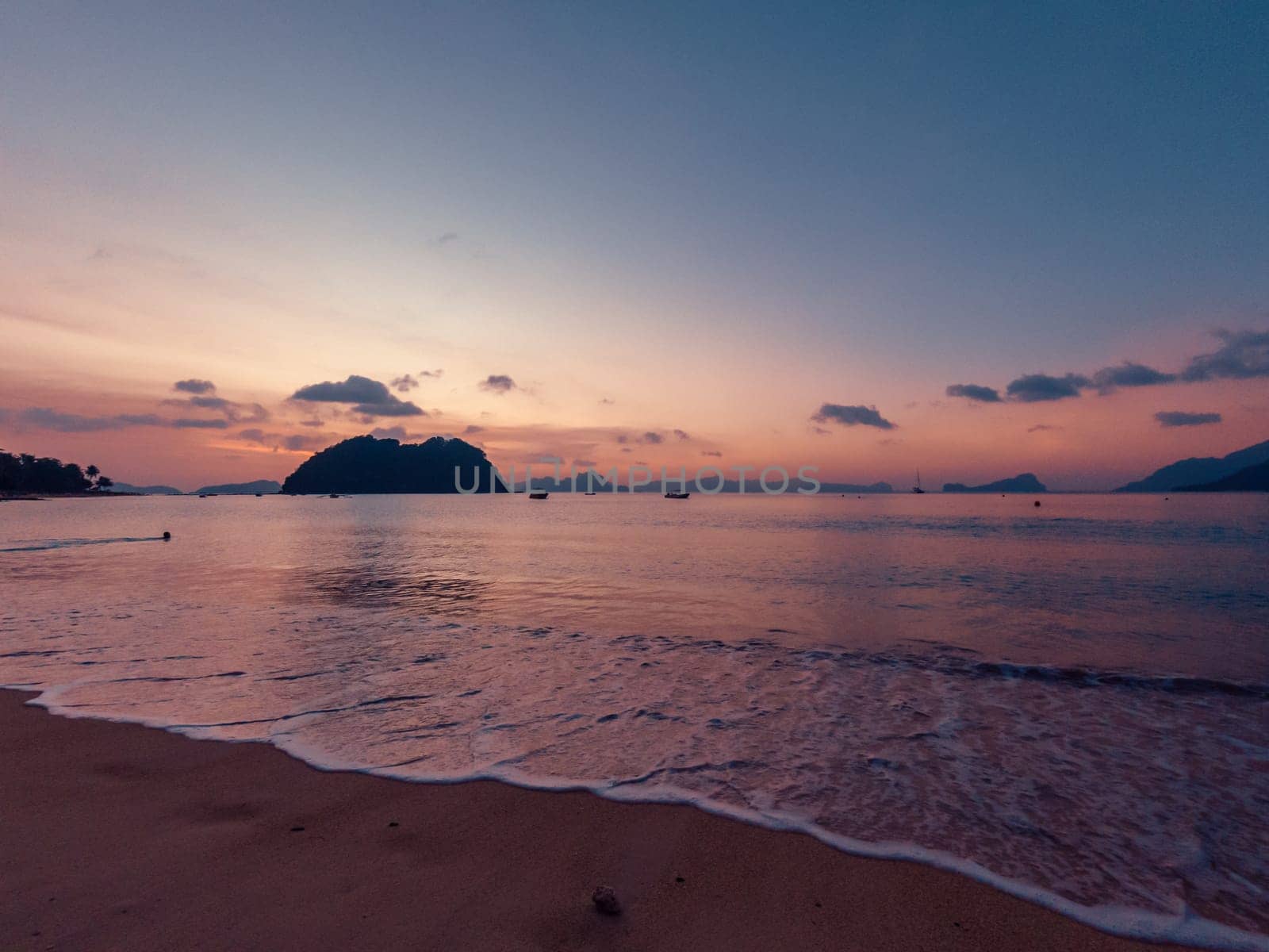 Gorgeous sunset over tranquil beach with islands and boats at dusk by Busker