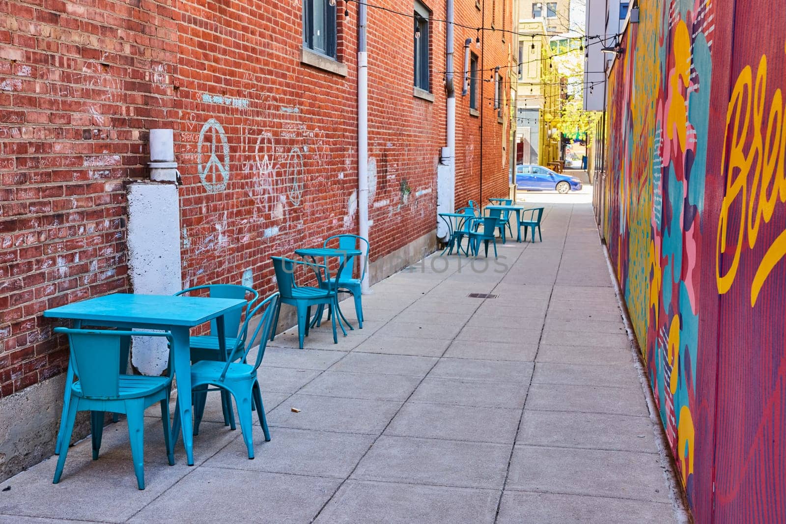 Vibrant alley in downtown Fort Wayne with colorful mural and turquoise cafe seating, showcasing urban renewal.