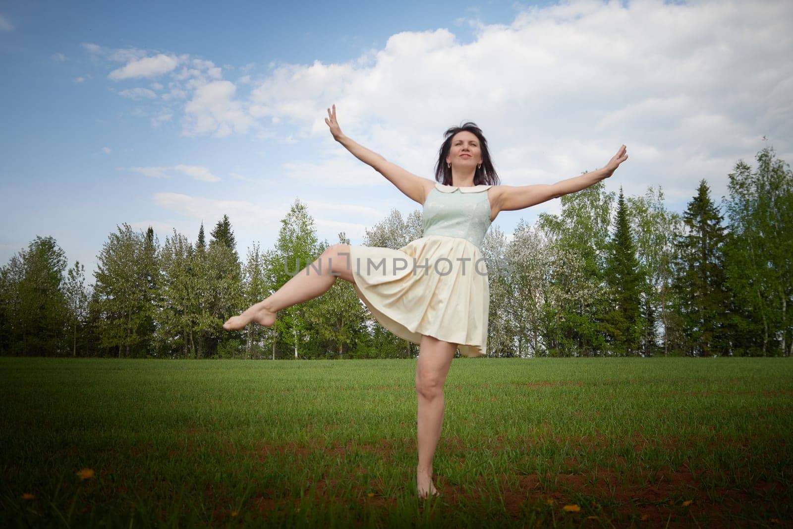 A beautiful young funny woman does sports or dance exercises in nature. A girl at a photo shoot in the landscape in spring or summer by keleny