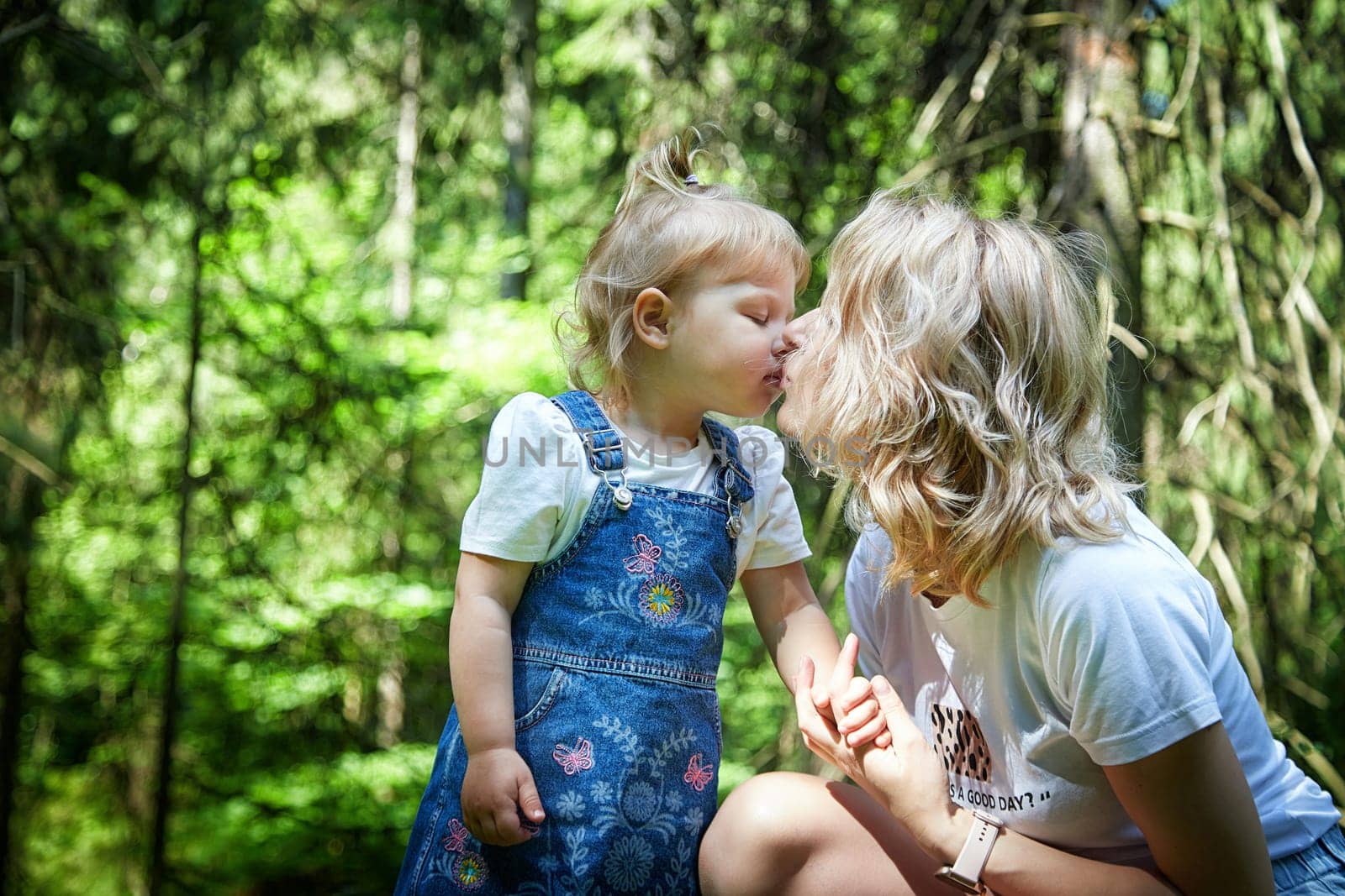 A mother and young daughter sharing a loving gaze among vibrant green trees