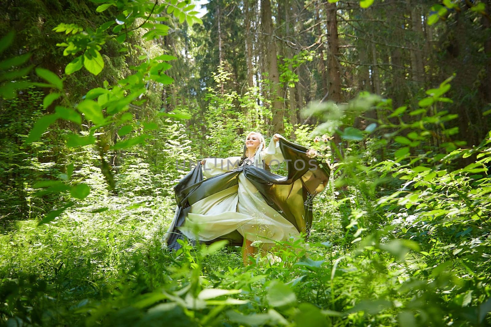 Adult mature woman 40-60 in a green long fairy dress in forest. Photo shoot in style of dryad and queen of nature. Fairy in beautiful green summer forest. Concept of caring for nature