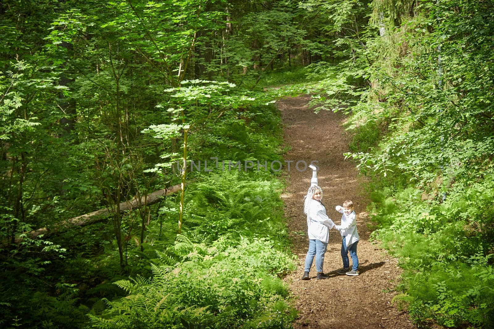 Funny mother with dreadlocks and fat boy happy walking in the forest on a sunny summer day