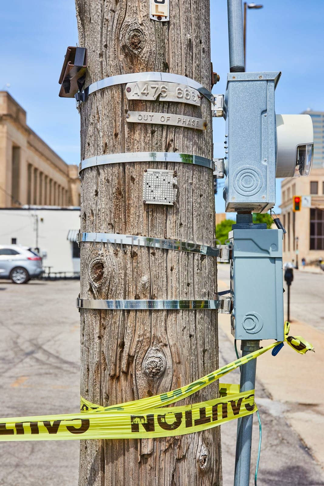 Sunlit utility pole in Fort Wayne, adorned with caution tape, an electrical box, and a traffic camera.