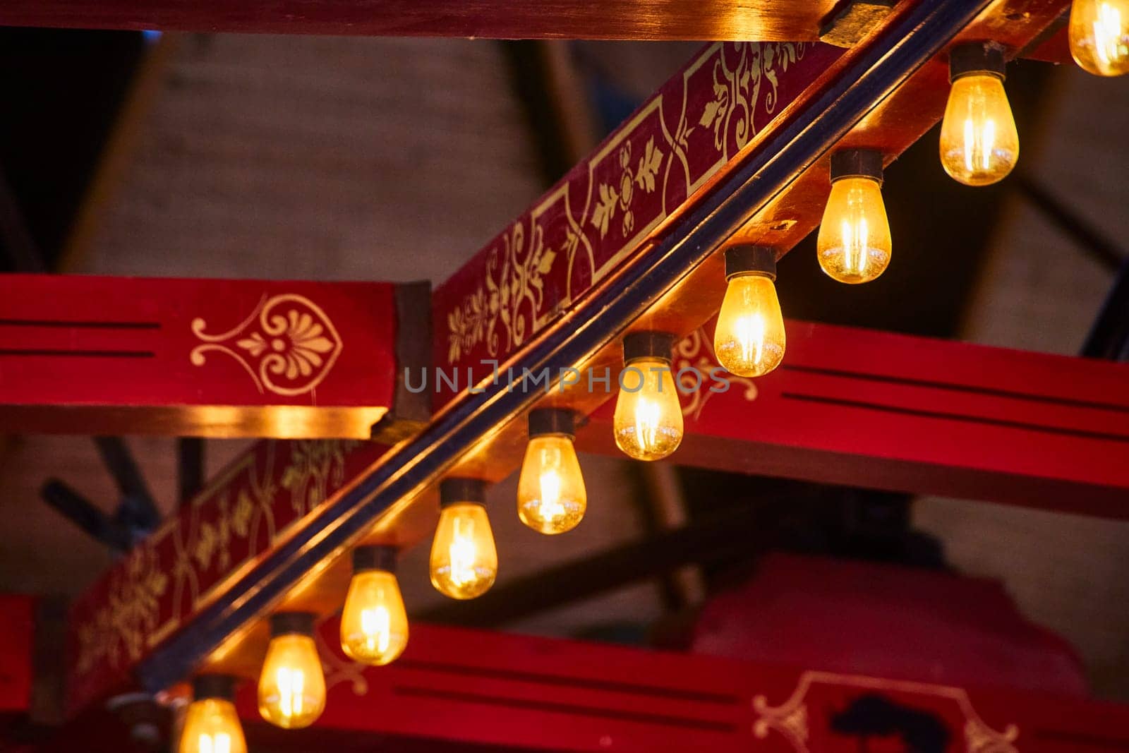 Warm Edison bulbs glow beneath a rich, red and gold railing, blending tradition with modernity in an intimate setting.