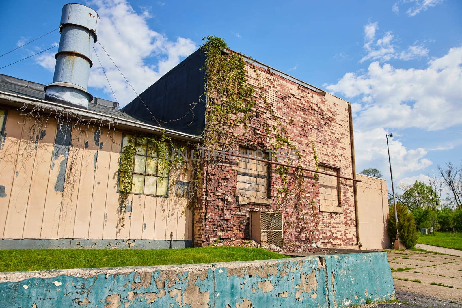 Abandoned industrial building with overgrowth in Warsaw, Indiana, under a clear blue sky.