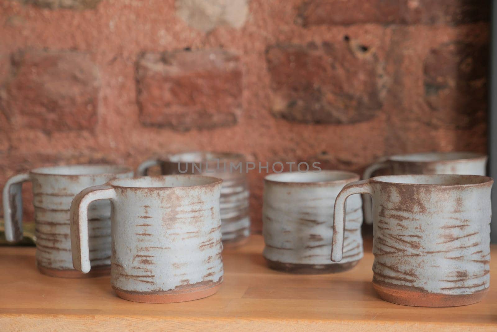 Tableware mugs displayed on hardwood shelf against brick wall by towfiq007