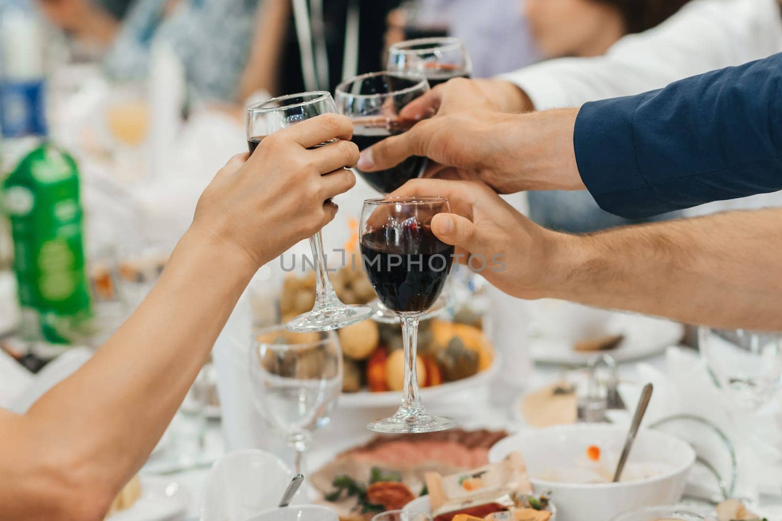 hands of a group of friends clinking glasses of wine and toasting and congratulating on a holiday in a restaurant