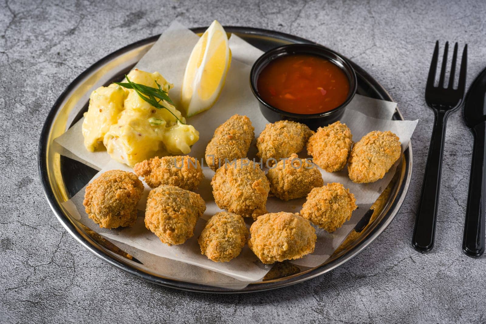 Fried mussels on a metal plate with potato salad on the side. Turkish name: Midye Tava