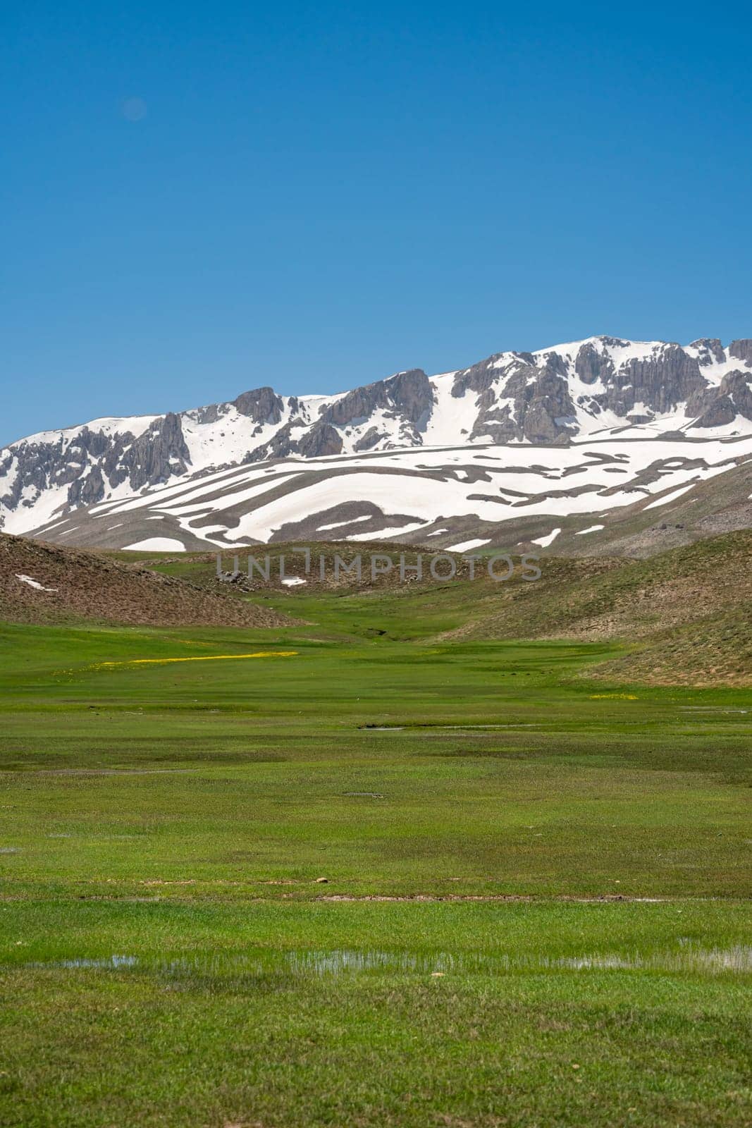 The lush green Sobucimen plateau in spring and the mountains with some melted snow behind.