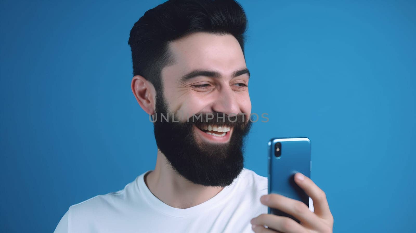 A happy man-a brunette with a beard, in a white shirt, standing isolated on a blue background, holding a smartphone in his hands. close up. Copy space