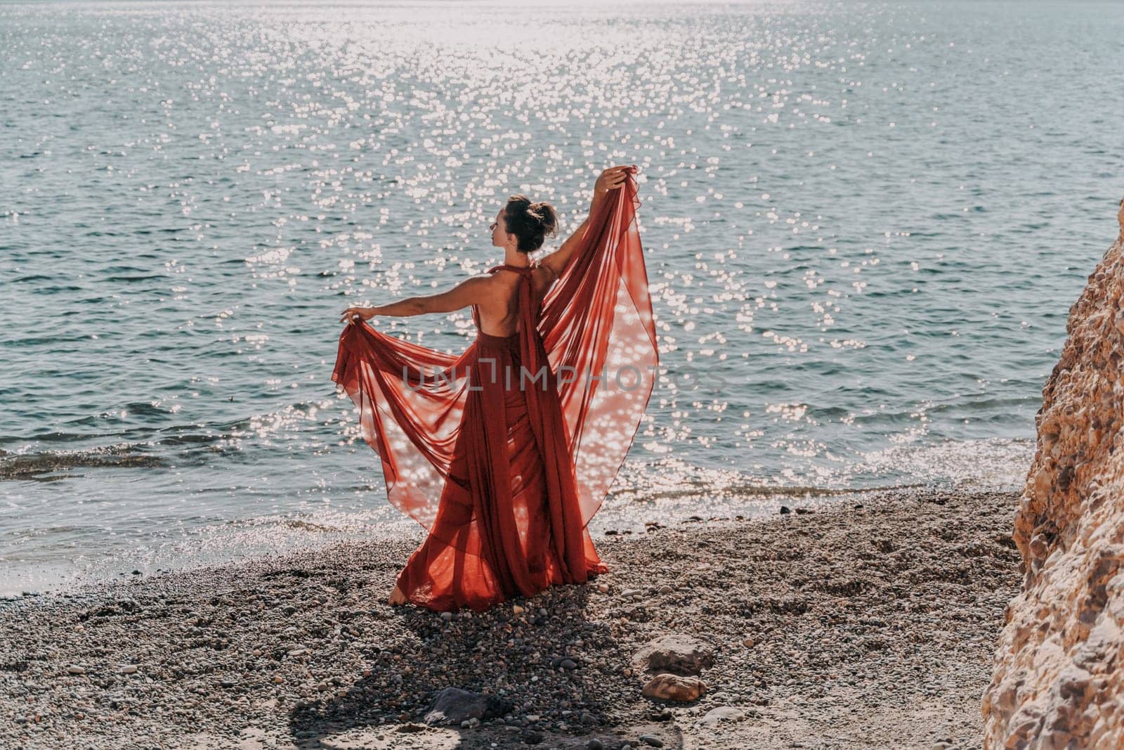 Woman red dress sea. Woman in a long red dress posing on a beach with rocks on sunny day. Girl on the nature on blue sky background. by Matiunina