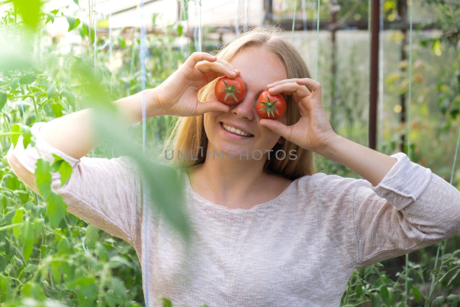 Smiling agriculture worker holding tomatoes over eyes in greenhouse. Fresh seasonal vegetables harvest. Food produce and cultivation. Sustainable by anna_stasiia