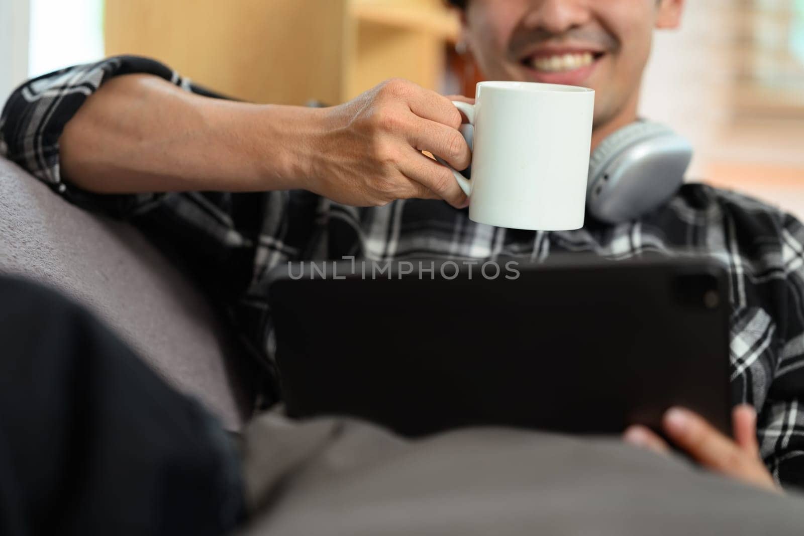 Smiling adult man drinking coffee and browsing Internet on digital tablet.
