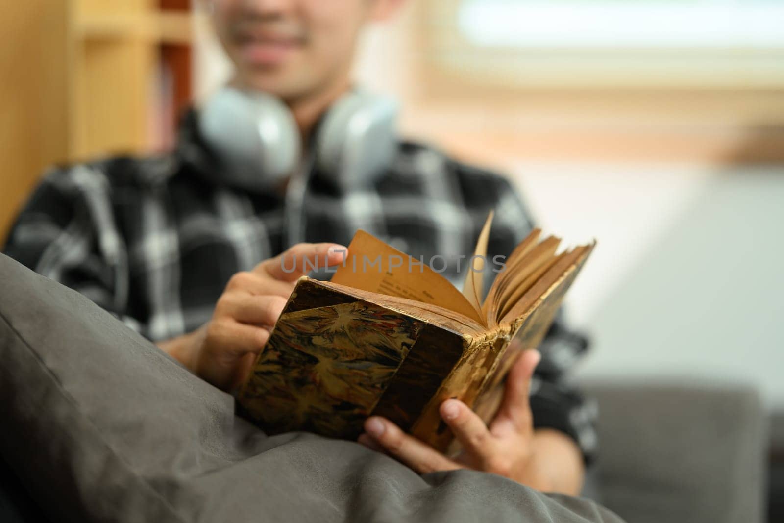 Young smiling man reading book on sofa spending leisure time at home.