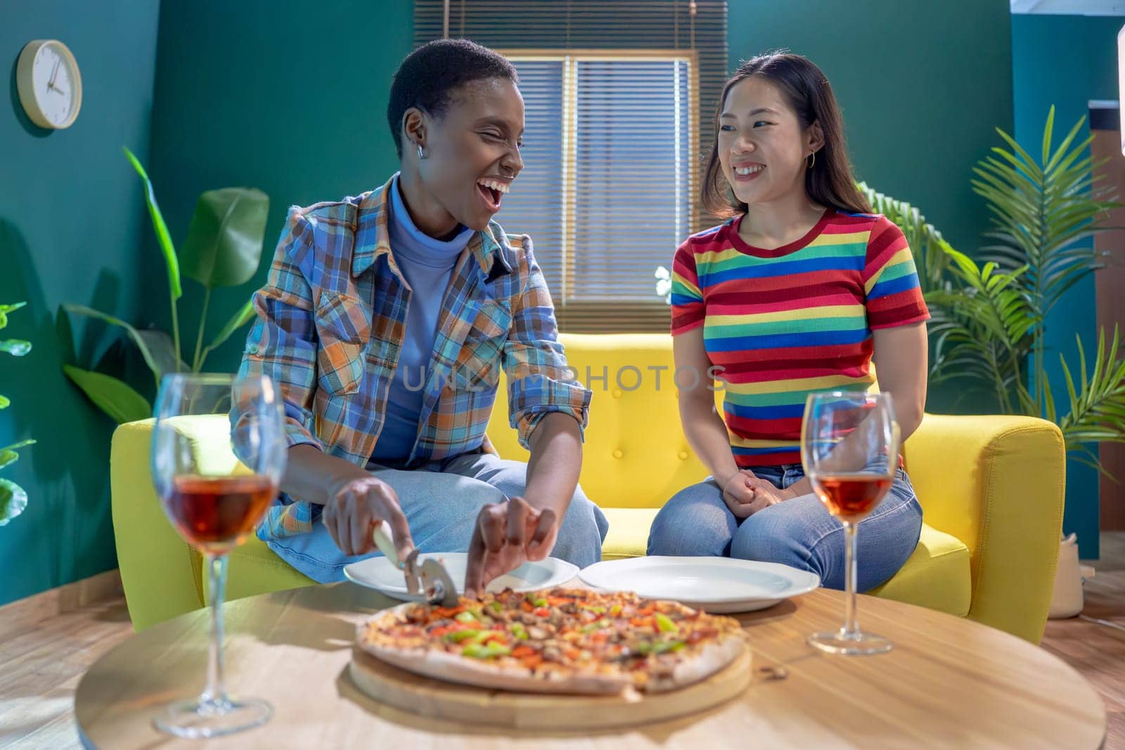 Two female friends celebrating with pizza and wine having fun together at home. High quality photo