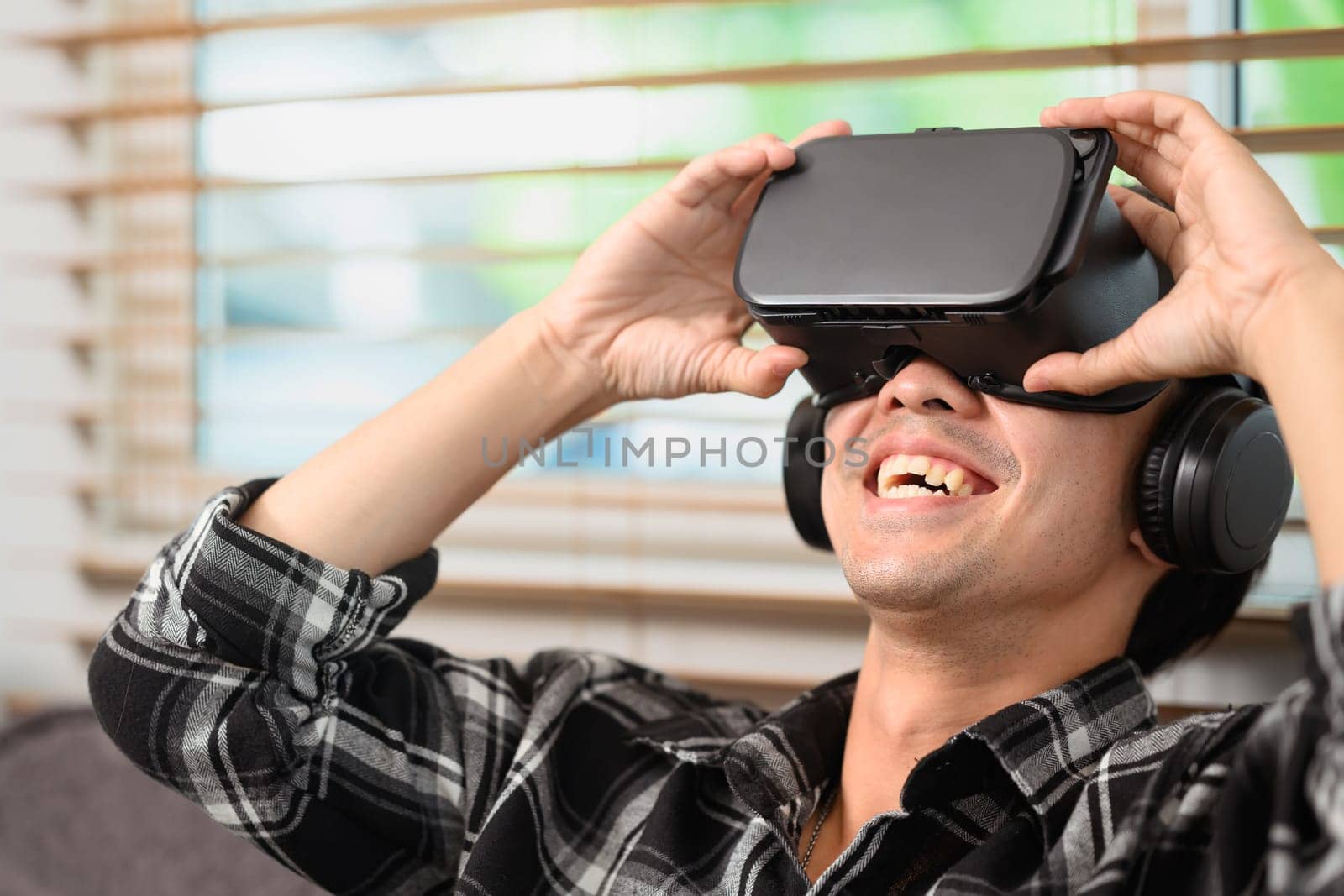 Excited man with VR headset sitting on a couch. Entertainment and virtual reality technology concept.