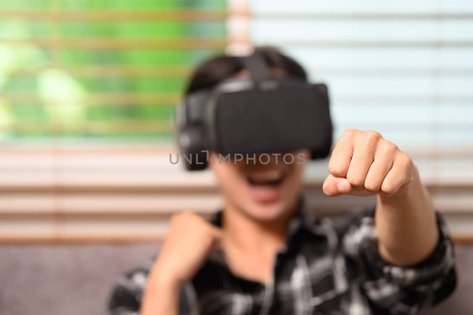 Joyful young man playing boxing game on virtual reality headset at home by prathanchorruangsak